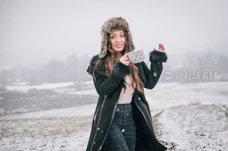 站在雪地上拿着一杯茶的年轻女子