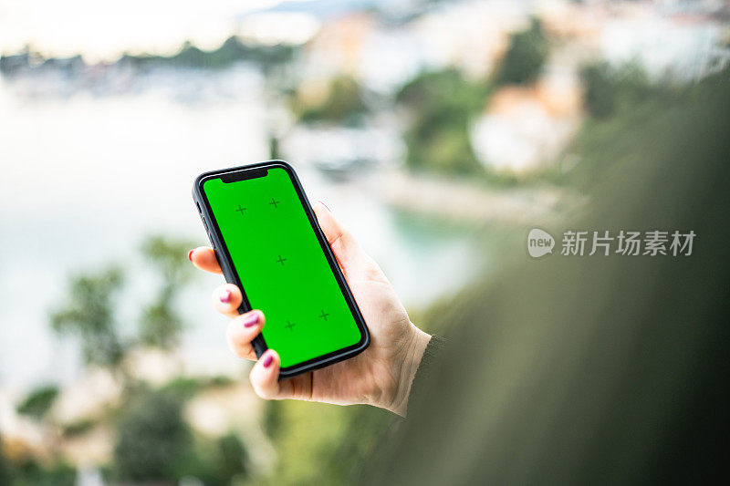 年轻的女孩使用手机与绿色屏幕在海边的阳台上的股票照片