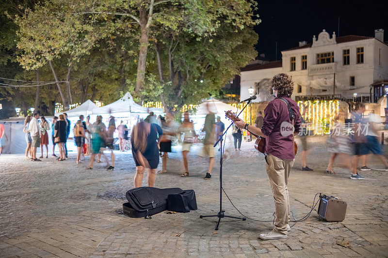 一名街头音乐家在一个度假小镇的广场上为路人演奏和唱歌。