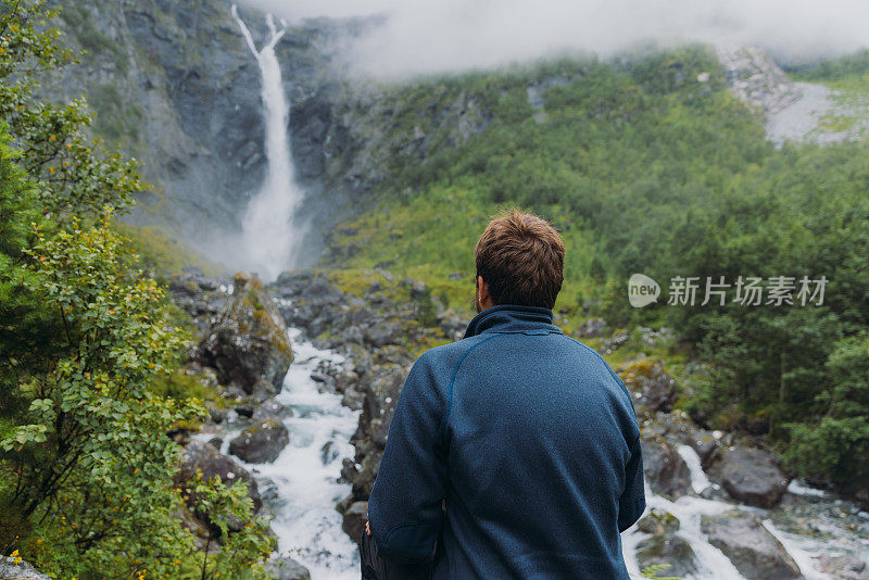 一个男人旅行者考虑在挪威瀑布风景山谷的后视图