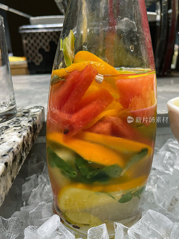 特写图片:玻璃罐中的水果、蔬菜和豆瓣菜叶水被冰包围在餐厅自助场景中，新鲜的夏季饮料，橙片、柠檬和红甜椒，排毒饮食，健康食品概念，重点放在前景