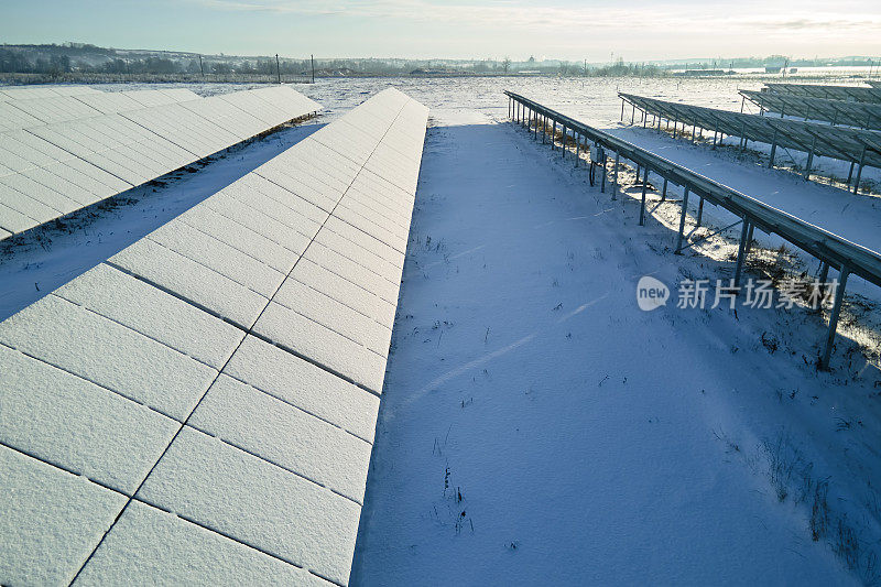 积雪覆盖的可持续发电厂鸟瞰图，该发电厂有成排的太阳能光伏板，用于生产清洁电能。北方冬季可再生能源发电效率低