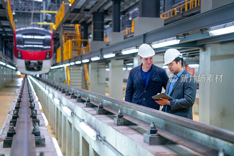 在工厂的电气或地铁列车前，职业经理或工程师工人在铁轨旁与平板电脑一起讨论。