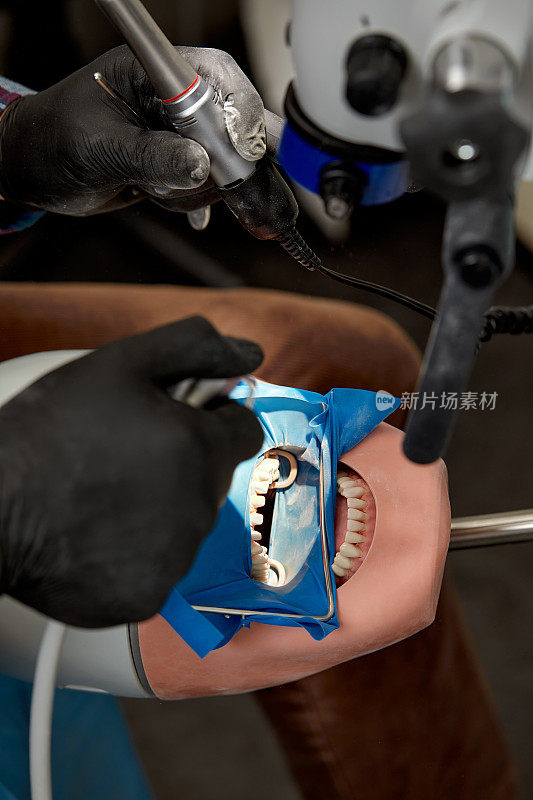 俯视图牙医的手谁正在学习治疗人类头部假人的牙齿。戴着黑色无菌手套的医科学生的手拿着牙钻。口腔医学和正畸学的概念。