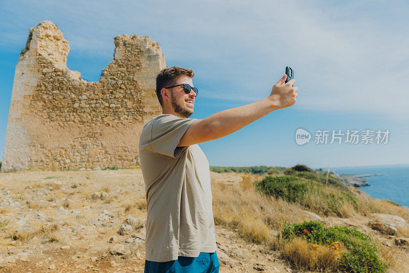 男子旅行者用智能手机拍摄意大利普利亚波尔图塞尔瓦吉奥国家公园的老堡