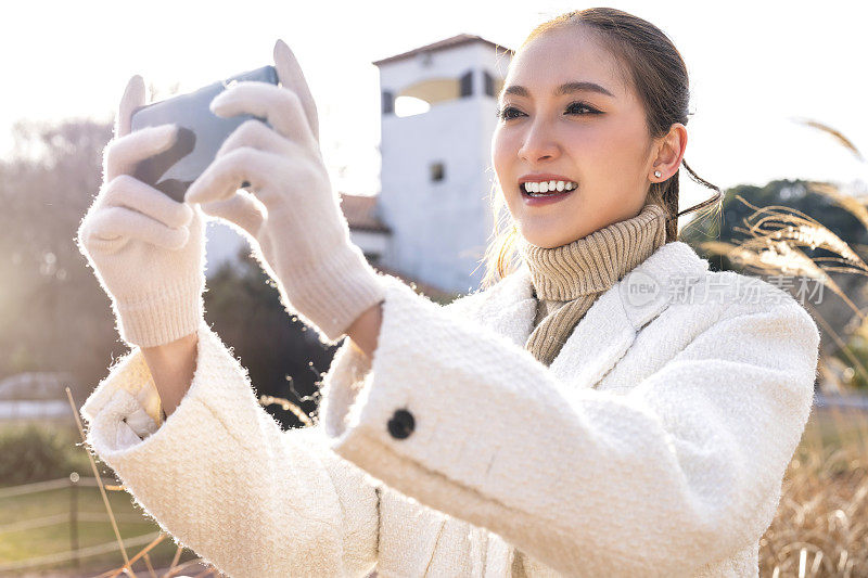 迷人的亚洲女性旅行者休闲布手拍照与智能手机设备，而一日游独自旅行与草地草地迷人的地方日落背景