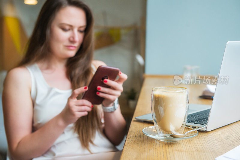 专注于一杯咖啡与模糊的商业女性女企业家在咖啡馆用笔记本电脑工作时发短信，共同工作。远程工作，社交网络，博客。远程办公的概念。