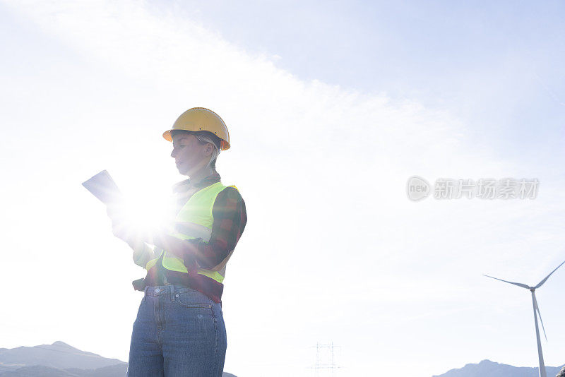 一名女工程师正在检查用于可再生能源生产的风力涡轮机基础设施，她正在使用数字平板电脑记录现场数据