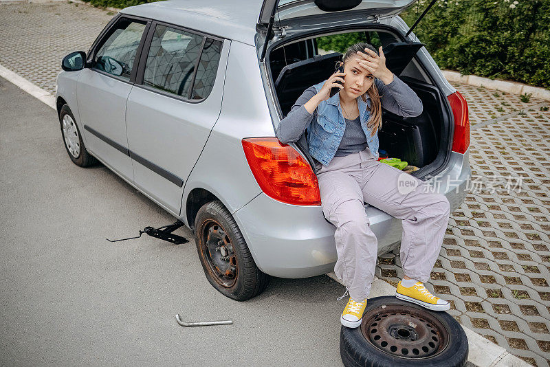 一名女子坐在车后座上用手机求助，因为她的车胎爆了