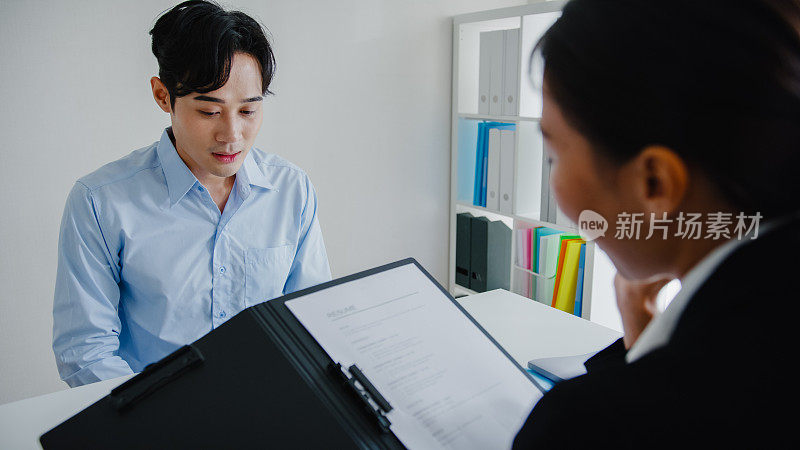 一个年轻的亚洲人通过了面试，坐在办公室的人力资源经理面前。人力资源，招聘机构。