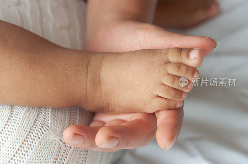 一个温柔的时刻，新生儿的小脚被大人的手抱着，象征着关心和爱。