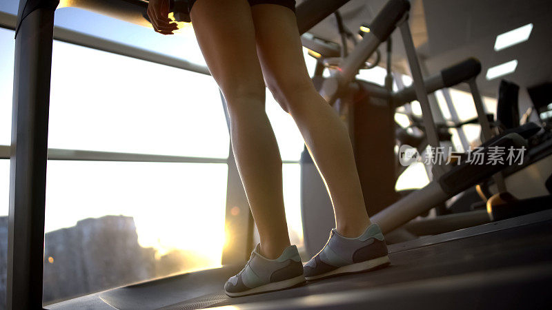女性站在健身房里的跑步机上，在锻炼前享受日出