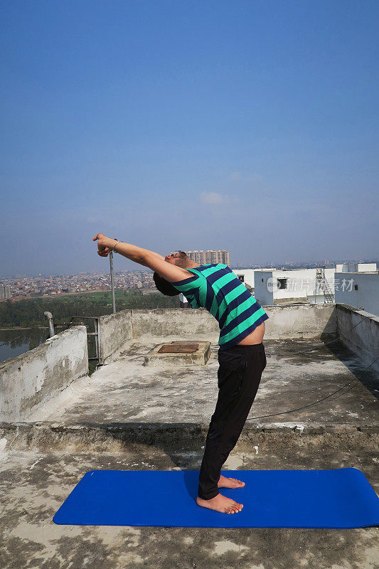 印度人在屋顶上练习举起手臂(Hastauttanasana)瑜伽姿势的照片，德里，印度