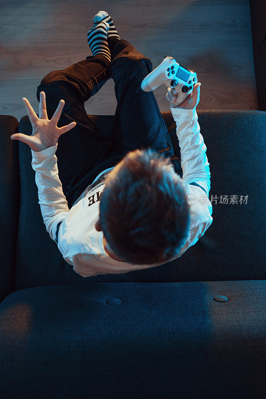 男孩晚上坐在沙发上玩电子游戏的高角度视图