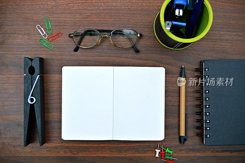 一个文具的横向照片，如钢笔，日记本，螺旋记事本，笔架与笔，订书机，眼镜放置在一个木制的深棕色水平背景上，非常美观。