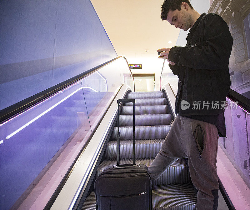 年轻的成年男子在机场的自动扶梯上使用手机
