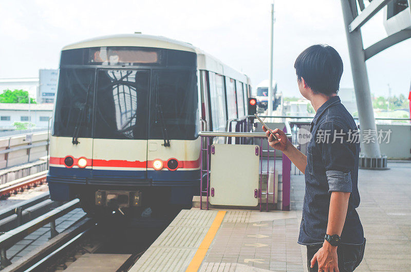 亚洲男子乘客使用智能手机在火车站看BTS，在BTS轻轨站等待。
