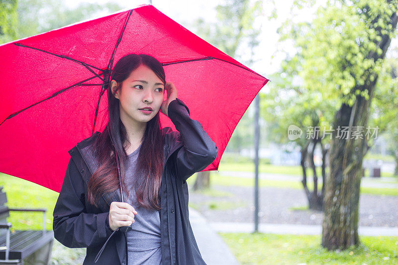 美丽的亚洲女人看着一边拿着红伞走在雨中在一个公园