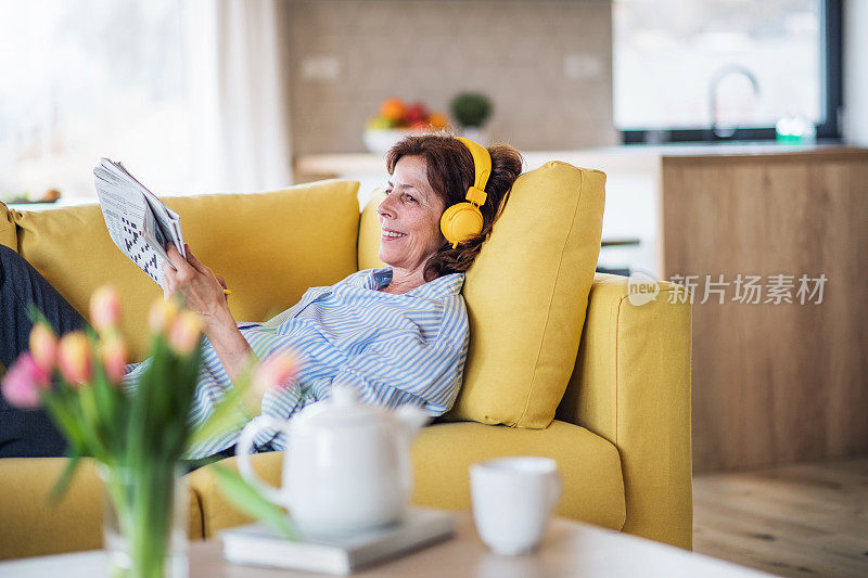 一位老妇人戴着耳机坐在家里的室内沙发上休息。