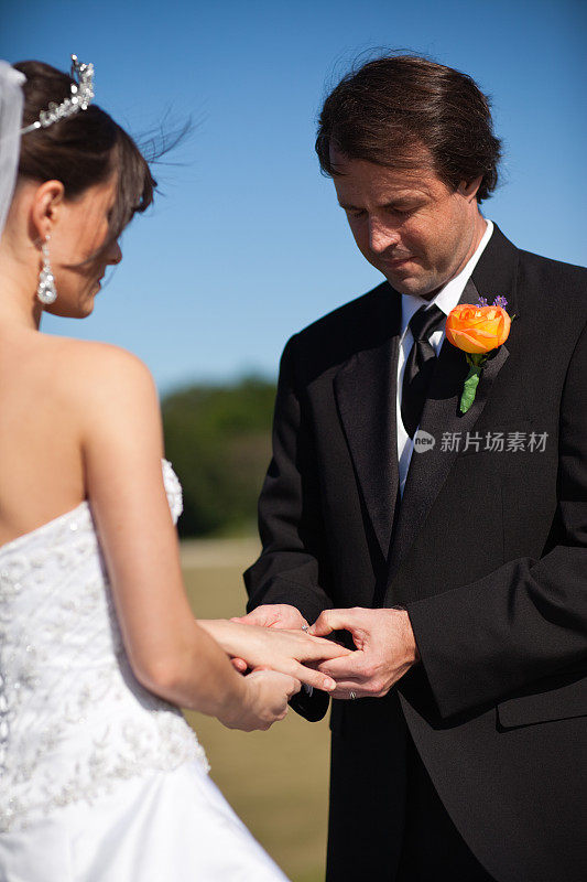 新郎将戒指戴在新娘手指上的彩色图像