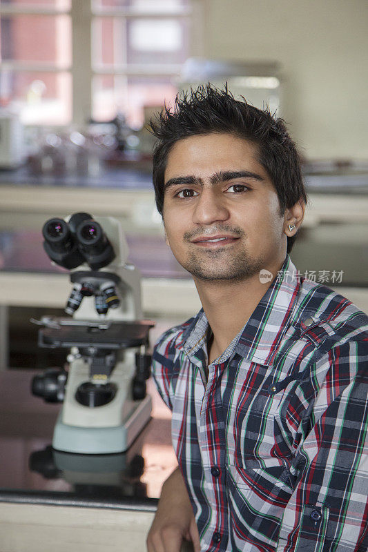 微笑的印度学生在实验室用显微镜观察