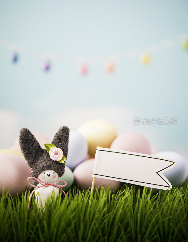 手工制作的复活节兔子与复活节彩蛋和空白旗帜在草地上