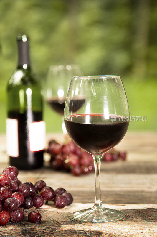 夏日红酒放在质朴的户外餐桌上。瓶,葡萄。
