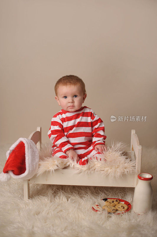 穿着圣诞睡衣坐在木床上的严肃婴儿