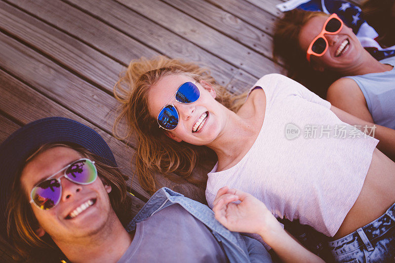 酷酷的少年朋友们戴着太阳镜躺在木制的甲板上微笑