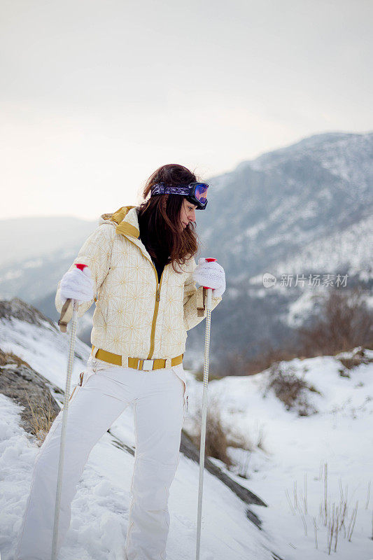 近景美丽的年轻女子在冬天的衣服站在一边，手拿木棍的背景雪山