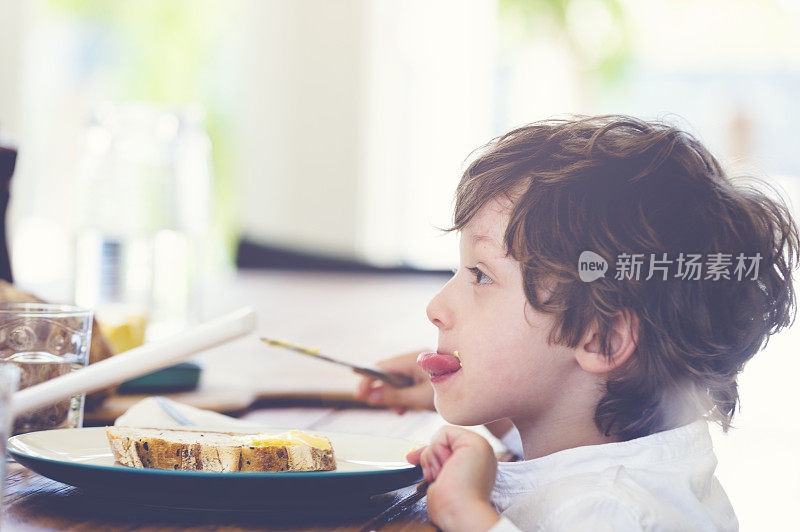 小男孩在桌子上吃面包。