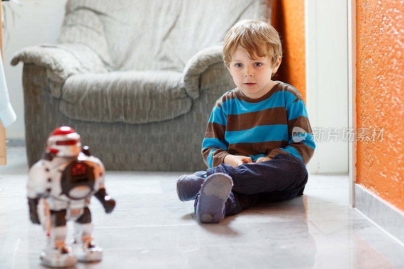 金发小男孩在家玩机器人玩具，在室内。
