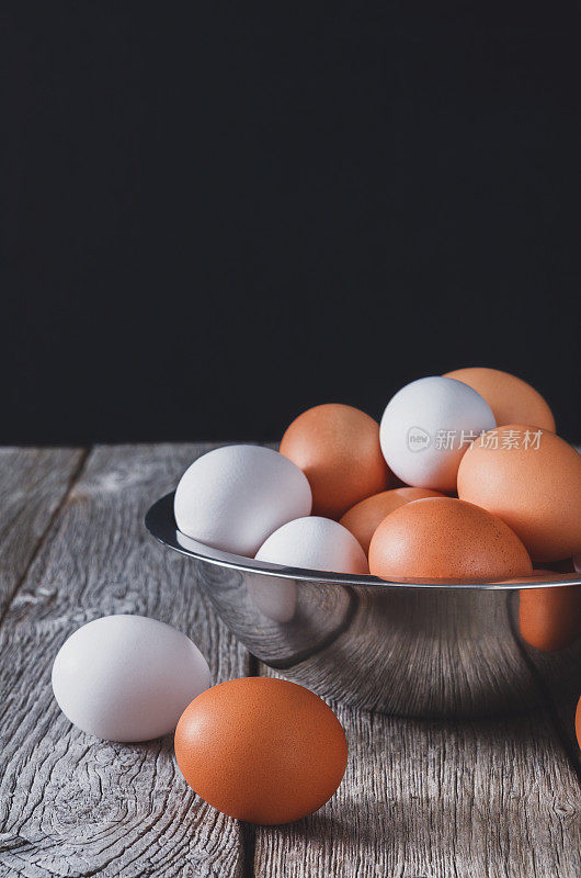新鲜的棕色鸡蛋放在碗里，黑色背景放在木头上