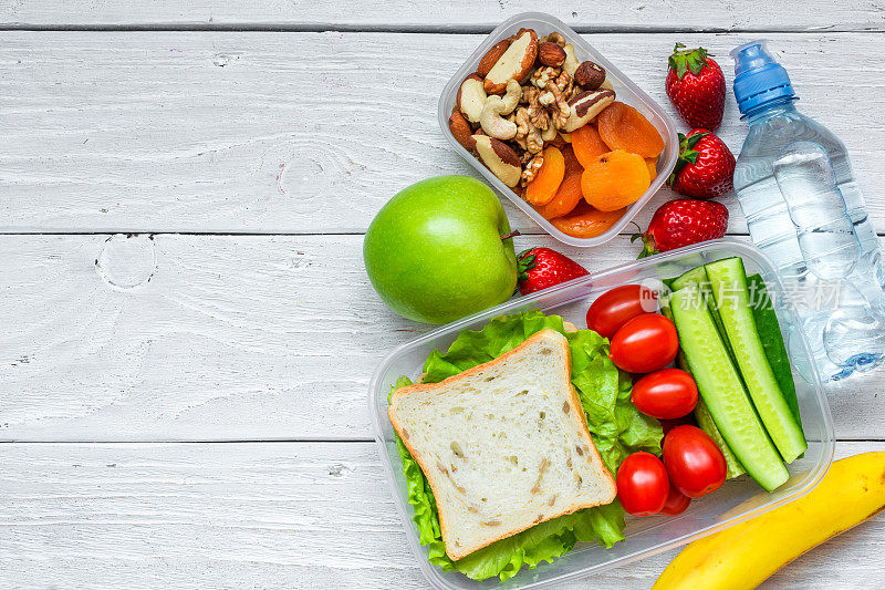 学校午餐盒有三明治和新鲜蔬菜，一瓶水，坚果和水果