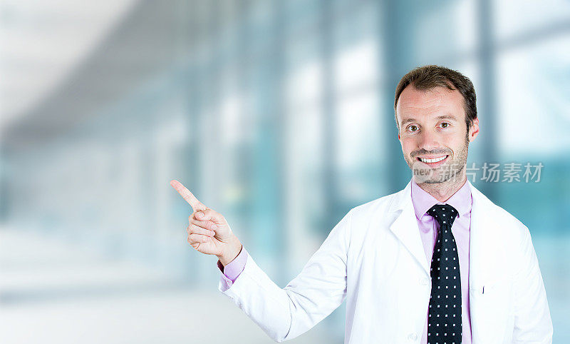 一个友好的快乐的男医生微笑着用手指指着医院的走廊