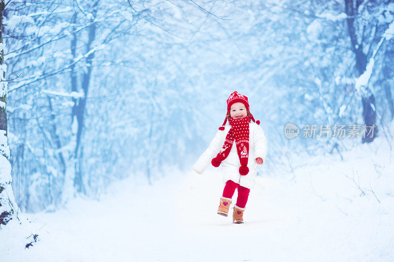 甜美的小女孩在白雪覆盖的公园里奔跑