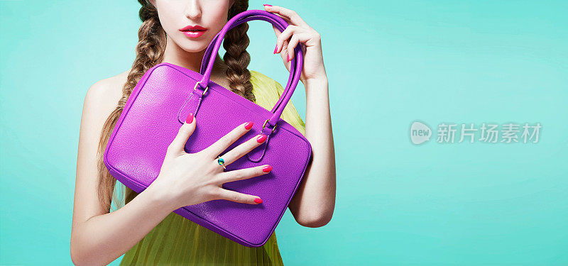 年轻的女孩拿着紫色的皮包钱包。孤立在明亮的水蓝色背景上。时尚物品的形象。