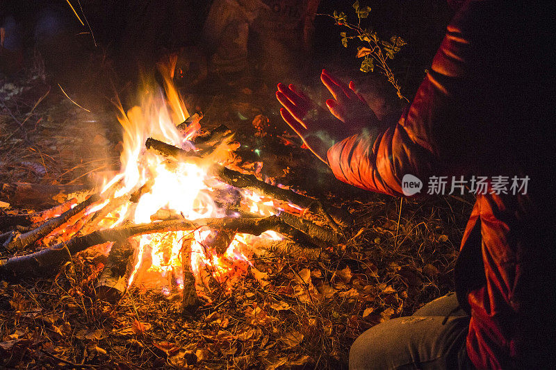 女孩在黑夜的森林里从火中温暖她的手