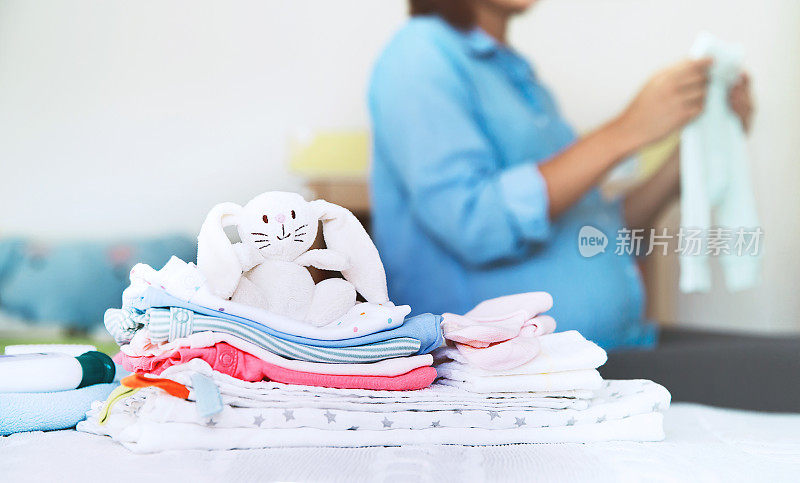 卧室室内家中床上堆满婴儿衣物、必需品和孕妇。