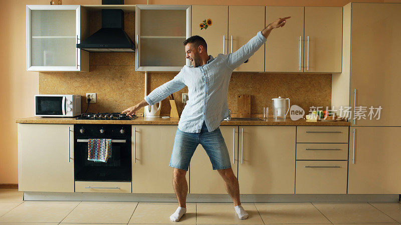 英俊的年轻有趣的男人在厨房跳舞在家里的早上和有乐趣的假期