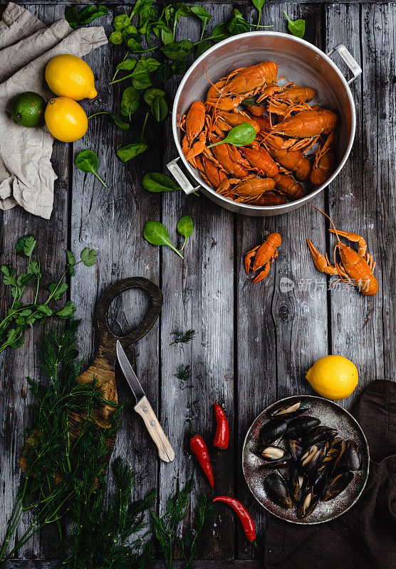 俯瞰平底锅里的龙虾和贻贝，质朴的木桌上放着香草和柑橘类水果