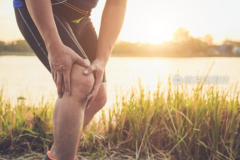 受伤的概念:亚洲男子在公园的道路上跑步时用手按住膝盖。拍摄于早晨时间，阳光和温暖的效果与复制空间的文字或设计