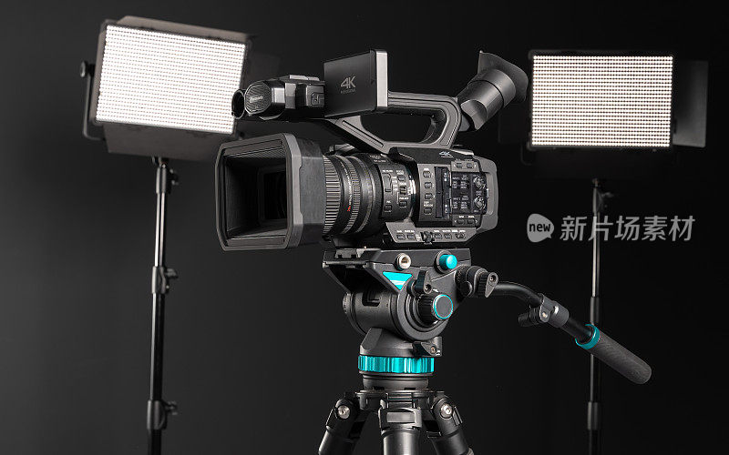 专业4K摄像机在相机三脚架和两个照明LED面板在黑色背景，侧视图