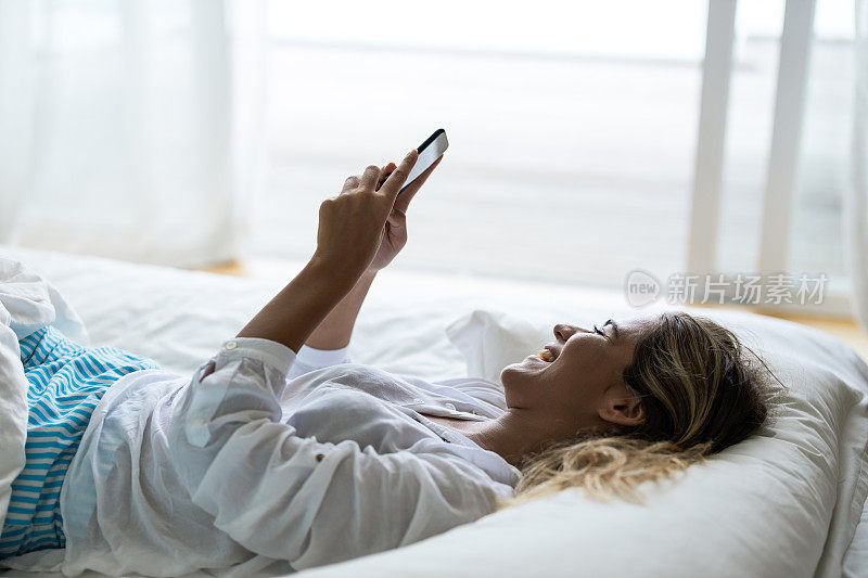 快乐的女人在床上放松用智能手机发短信。