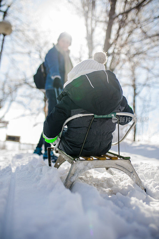 快乐的母亲和儿子在公园玩雪橇。