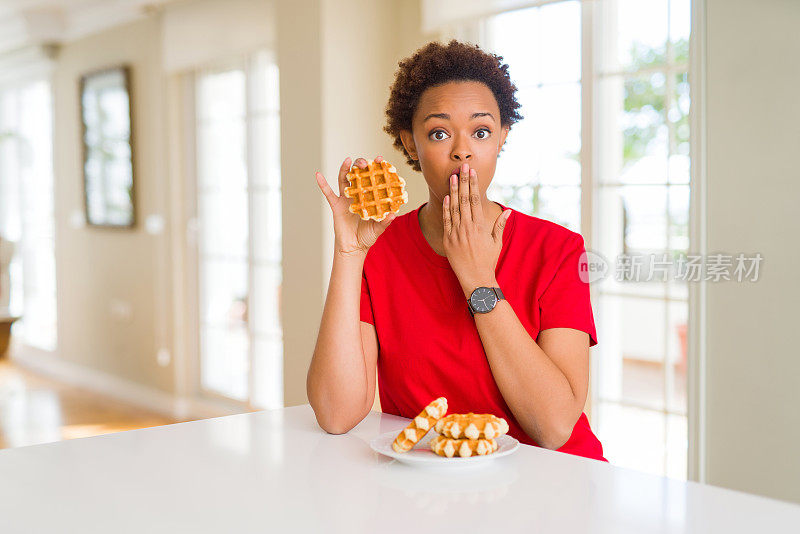年轻的非裔美国女子吃着甜华夫饼捂着嘴用手震惊，因为错误而感到羞愧，表情恐惧，在沉默中害怕，秘密概念