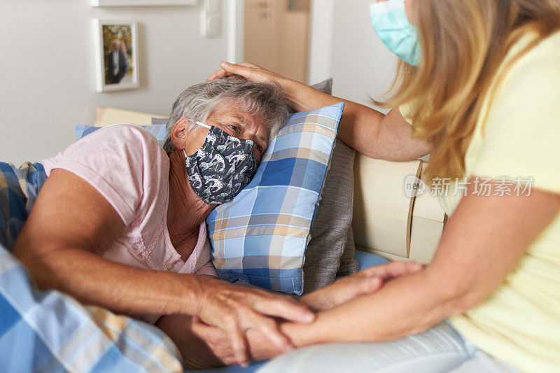 一个女儿和感染Covid-19病毒的母亲坐在床上，两人都戴着呼吸口罩或防护口罩