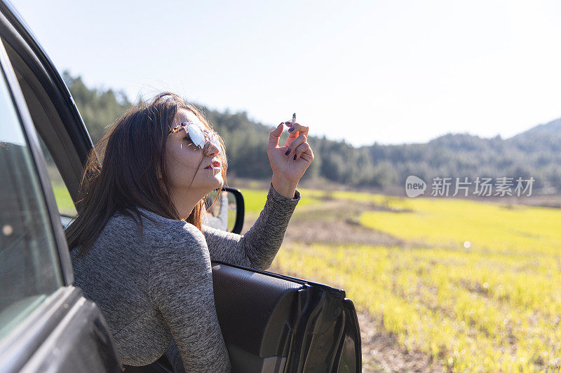 女人从开着的车门中望着自然，在路上抽着烟