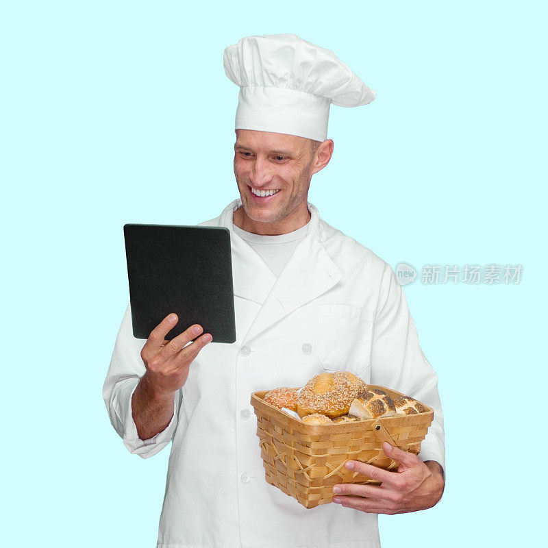 白色男性面包师前面的蓝色背景穿着制服，拿着一条面包和使用数字平板电脑