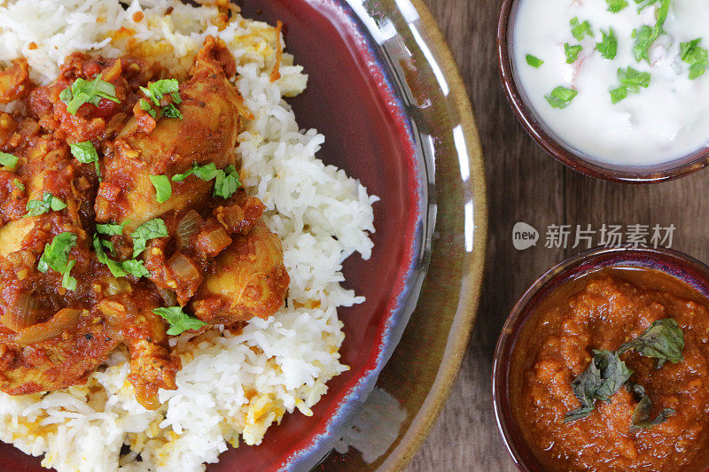 盘子的特写图像含有自制的印度外卖米饭菜鸡肉biryani在陶瓷盘子与raita酸奶肉汁为基础的酱汁，升高的观点
